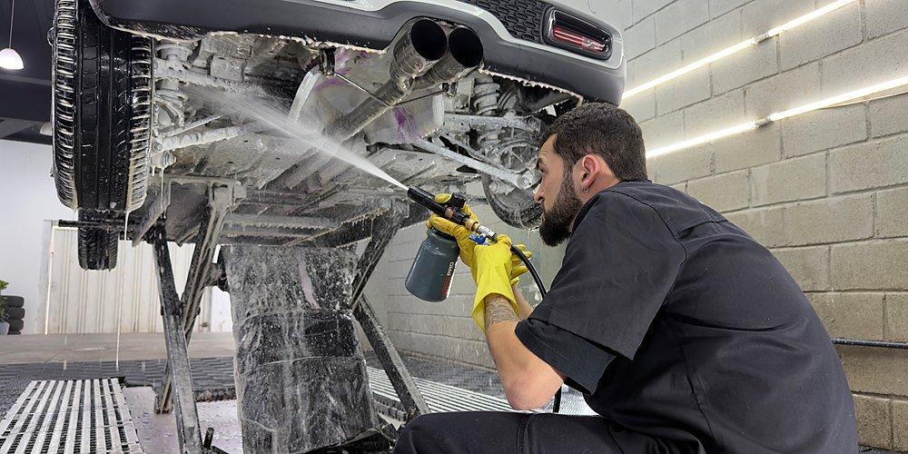 Profissional da Lasmar Car Detail higienizando o chassi de um carro com pulverizador e luvas amarelas